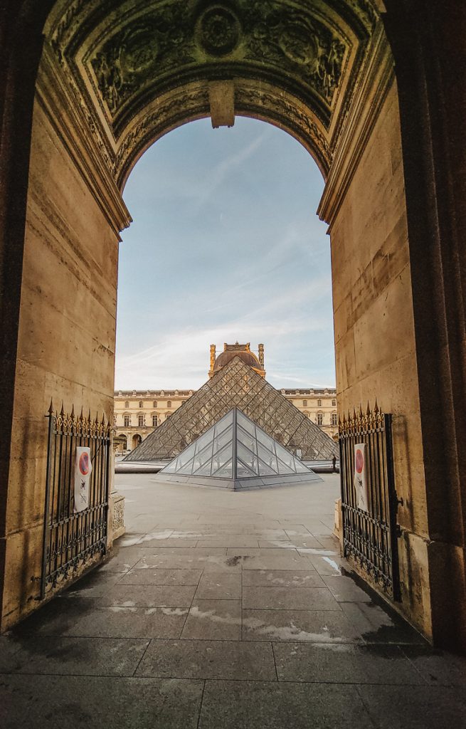 The view looking out at a glass triangle building with ornate buildings surrounding the courtyard
