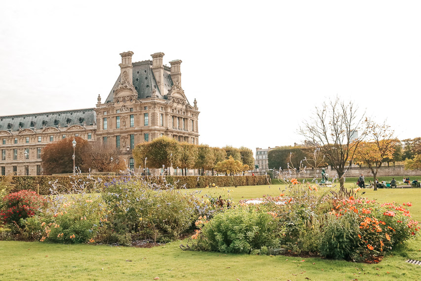 A lawn with flower beds on it, with a wing of the Louvre in the background. The Jardin de Tuileries is one of the best gardens in Paris you have to visit. 